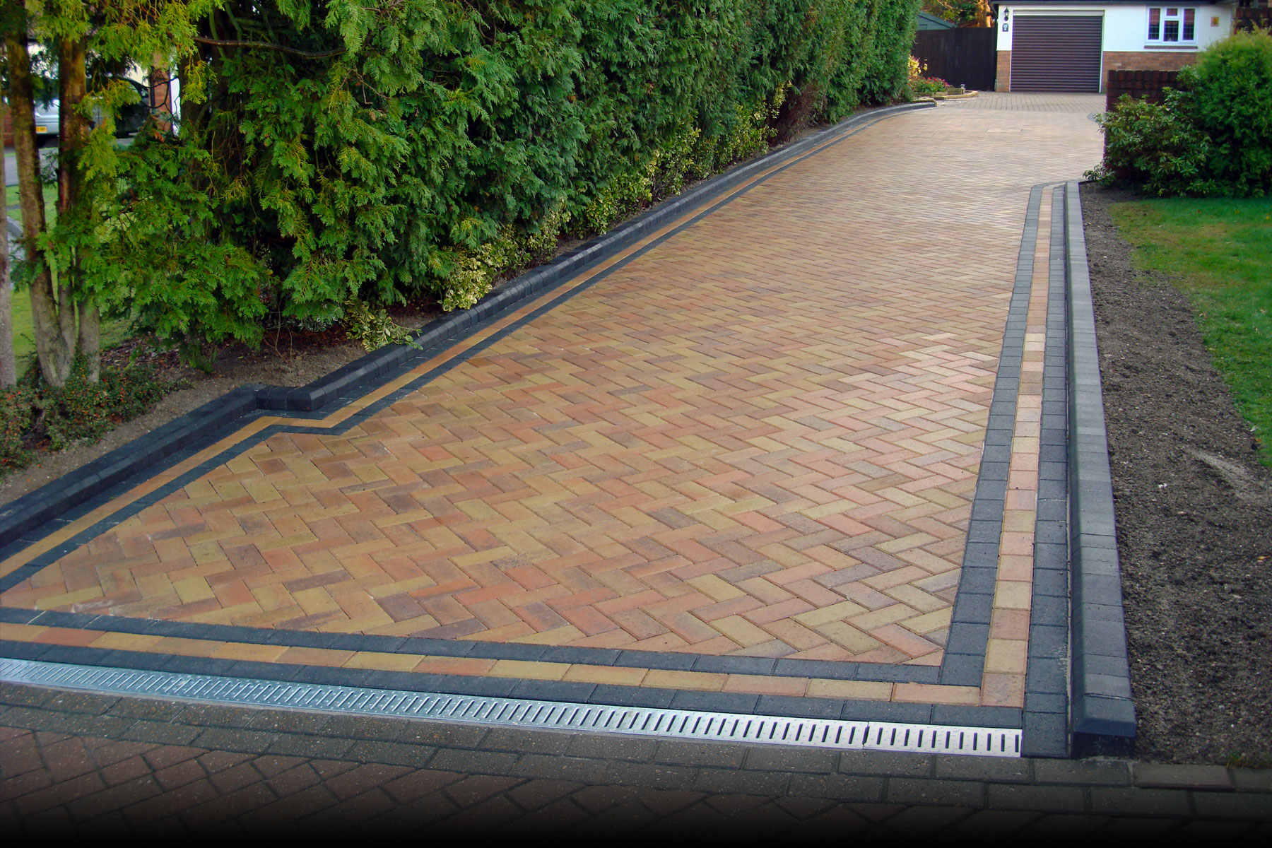 Chevron-paved-driveway-designs-with-nice-edging-and-living-fencing-green-yard-and-white-wall-coloring.jpg